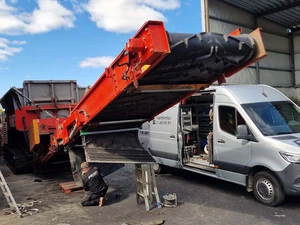 Technician repairing a chevron belt on a mobile waste sorting machine