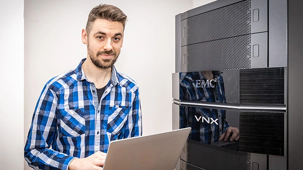Ein Auszubildender hält im Serverraum einen Laptop in der Hand.